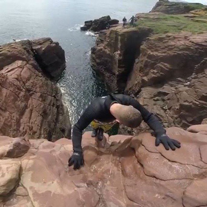 Chris Murphy on a cliff face preparing to cliff jump in his Northern Diver gloves and wetsuit